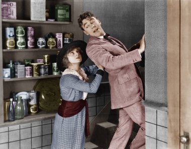 Profile of a young woman pushing out a young man from a domestic kitchen