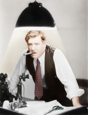 Man leaning over a desk with a ceiling light shining on him clipart