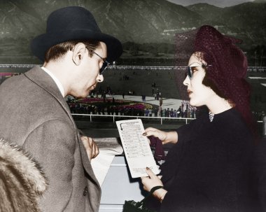 Elegant couple at a horse race looking at a program clipart