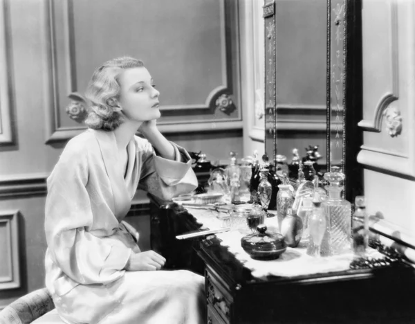 Женщина сидит на своем тщеславии, глядя в зеркало — стоковое фото