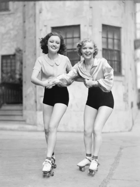 Dos mujeres jóvenes con patines patinando en la carretera y sonriendo —  Fotos de Stock