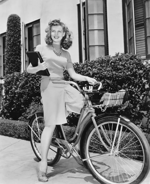 Mulher sentada na bicicleta com um livro nos braços — Fotografia de Stock