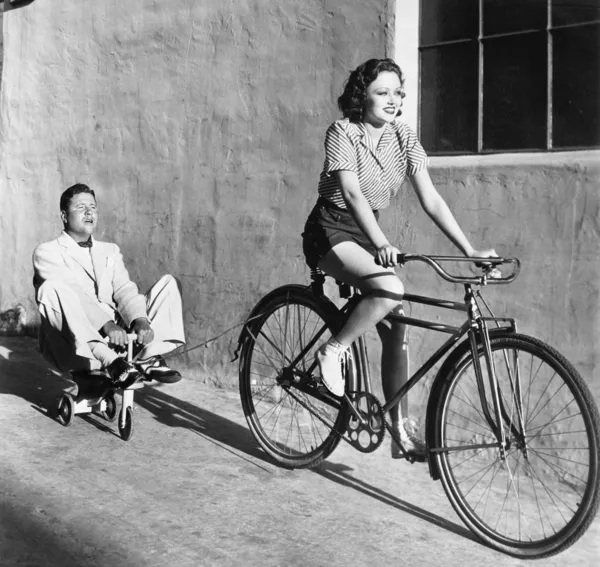 一辆自行车骑着玩具三轮车拉一个成年的男人的女人 — 图库照片