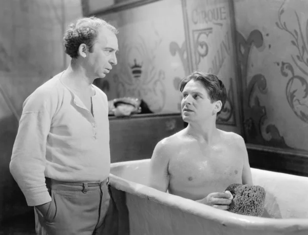 Двое мужчин разговаривают, когда один сидит в ванной — стоковое фото