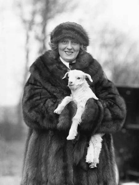 Kvinna i en päls kappa och hatt som håller en liten baby lamm i famnen — Stockfoto