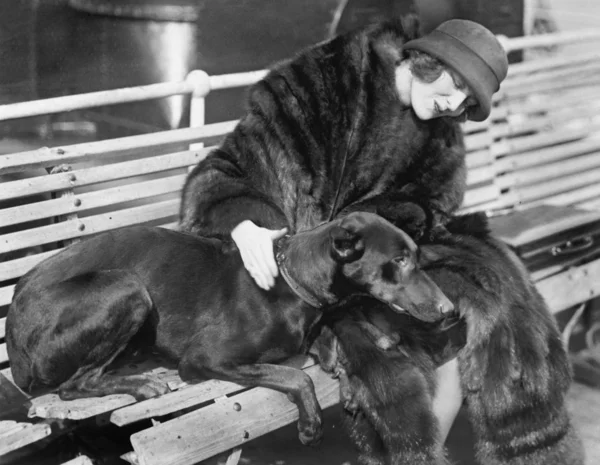 Frau im Pelzmantel sitzt auf einer Bank und streichelt ihren Hund — Stockfoto