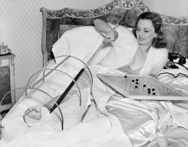 Vrouw in bed proberen te krabben haar gebroken voet met een pool — Stockfoto