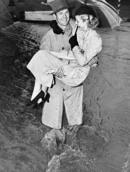 Young man carrying a woman through a rainstorm — Stock Photo, Image