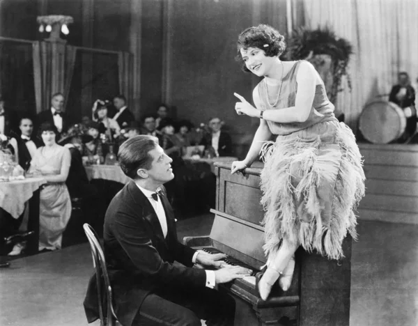 Mujer joven sentada en la parte superior de un piano y hablando con el pianista — Foto de Stock