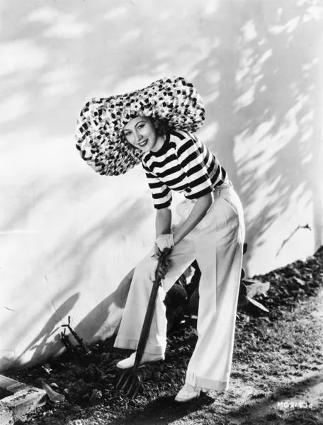 Mujer con sombrero de gran tamaño excavando en el jardín — Foto de Stock
