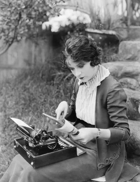Женщина сидит во дворе с пишущей машинкой на коленях — стоковое фото