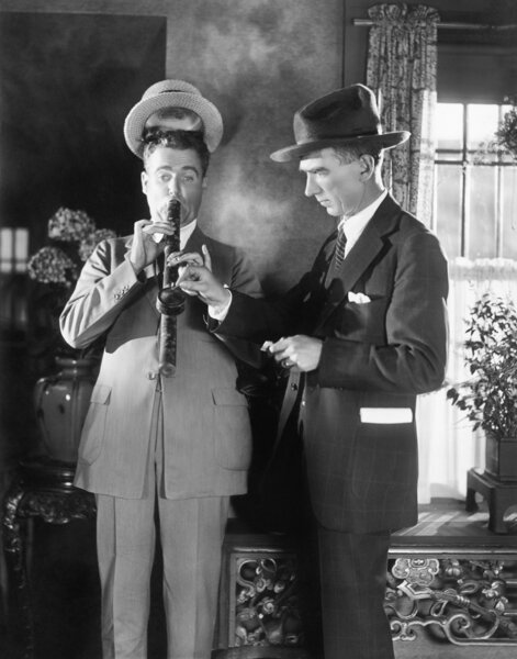 Человек зажигает длинную трубу, пока его шляпа поднимается с головы
