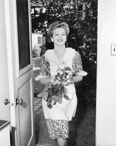 Donna che cammina attraverso una porta con fiori in mano — Foto Stock