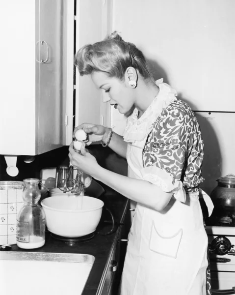 Женщина на кухне разбивает яйцо — стоковое фото