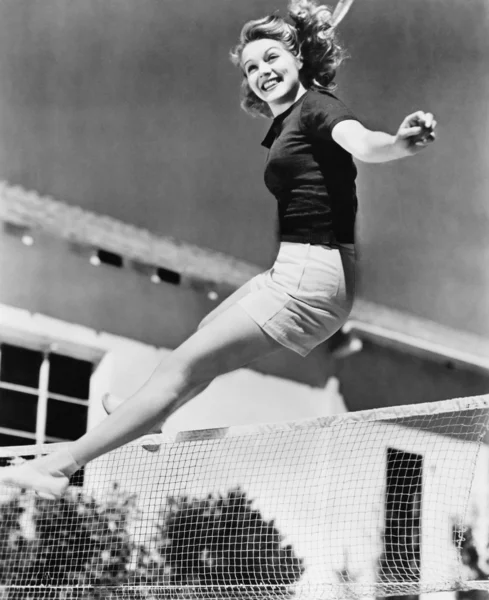 Mulher pulando sobre uma rede de tênis — Fotografia de Stock