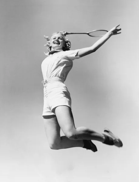 Kobieta skoki w powietrzu z rakietę tenisową w dłoni — Zdjęcie stockowe