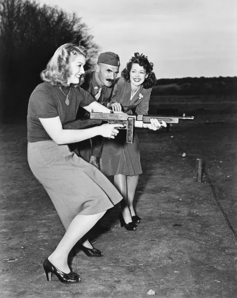Zwei junge Frauen und ein Soldat probieren ein Maschinengewehr aus — Stockfoto