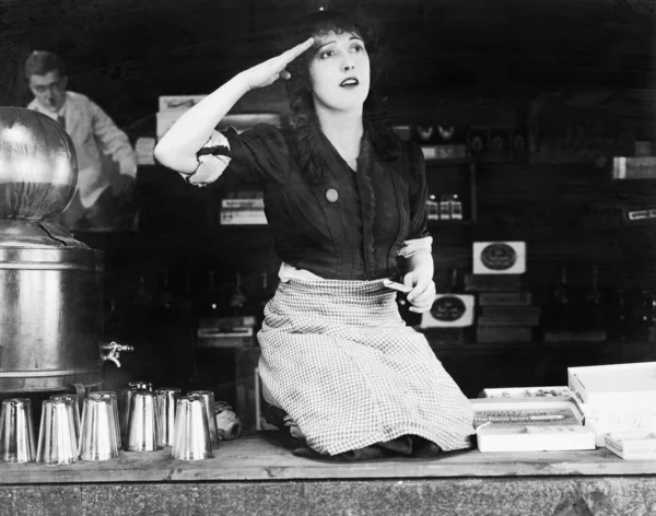 Woman kneeling on the counter of a bar and saluting — Stock Photo, Image