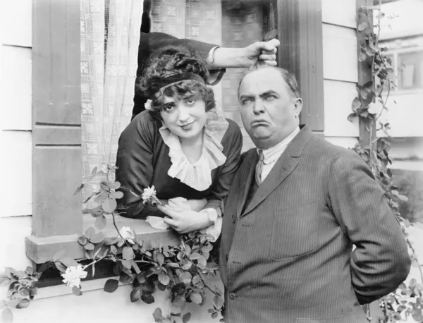 stock image Man having his hair pulled by a hand coming out of a window while standing next to a woman