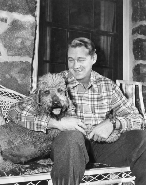 柳細工の家具に彼の犬と一緒に座っている男 — ストック写真