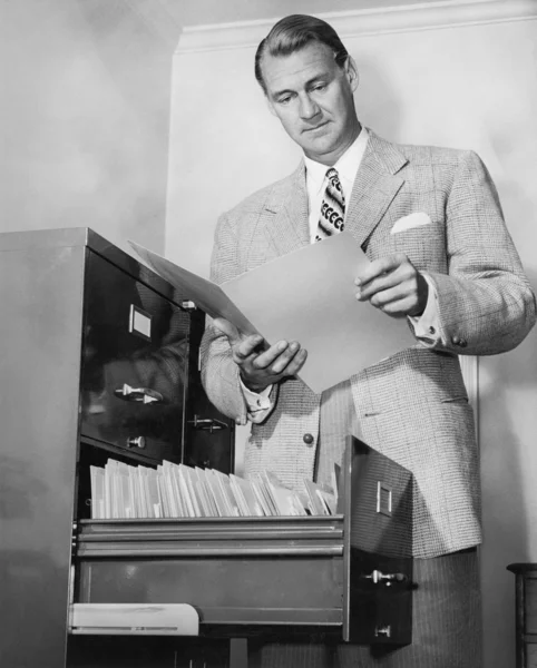 Бизнесмен смотрит на газету рядом с картотекой — стоковое фото
