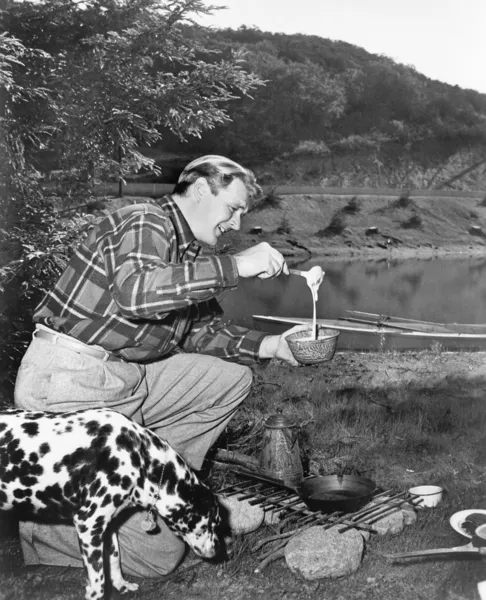 Muž a jeho pes kemp a přípravě potravin — Stock fotografie