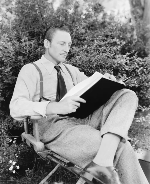 Homem sentado em seu jardim lendo um livro — Fotografia de Stock