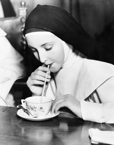 ストローで茶碗のお茶をすすりながら修道女 — ストック写真