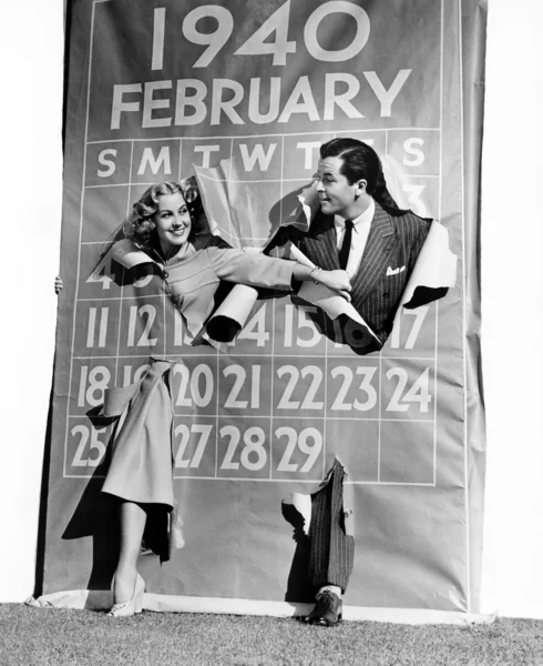 Casal estourando através do calendário ano bissexto — Fotografia de Stock