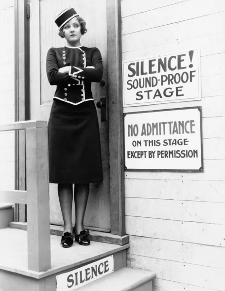 Young woman in a uniform standing with her arms crossed in front of a closed door — Stock Photo, Image