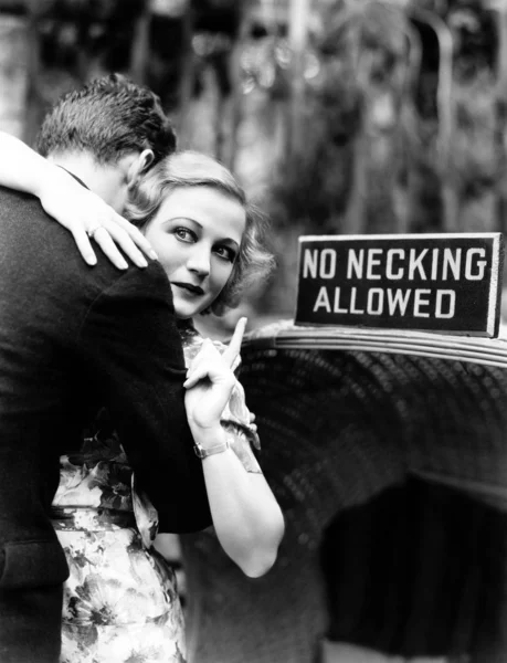 Jovem mulher abraçando um homem e apontando para um quadro de informações — Fotografia de Stock