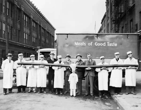 Carniceros mostrando una salchicha larga delante de un camión — Foto de Stock