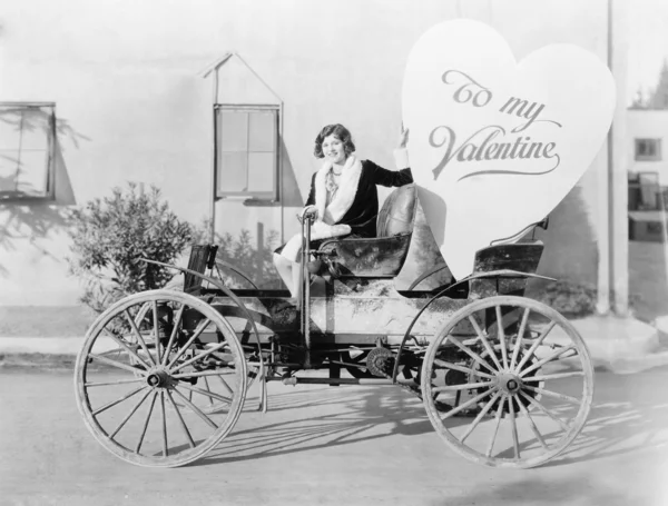 Młoda kobieta siedzi na samochód, posiadający wielkie serce w kształcie znak — Zdjęcie stockowe