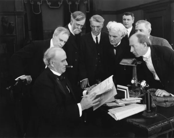 Hombres revoloteando alrededor del escritorio en anticipación de noticias — Foto de Stock