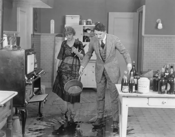 Man en vrouw die kijken naar gemorste vloeistof op de keukenvloer — Stockfoto