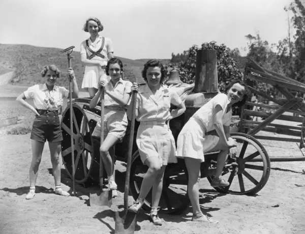 Mujeres jóvenes con herramientas de jardinería de pie cerca de carro de madera —  Fotos de Stock