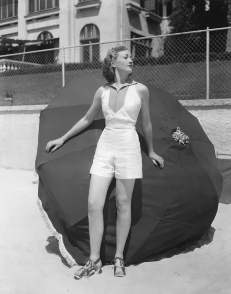 Женщина стоит перед пляжным зонтиком на пляже — стоковое фото