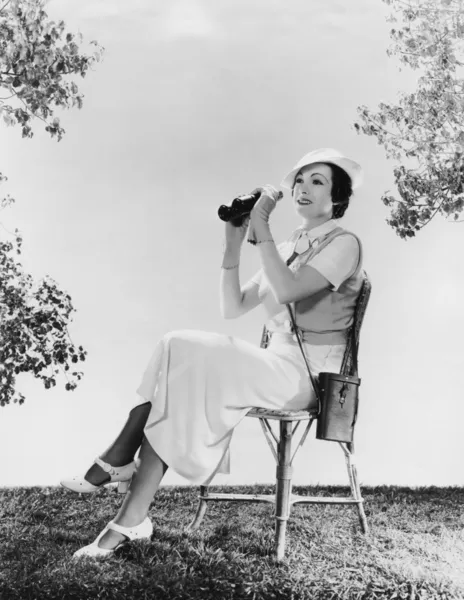 Елегантна жінка сидить на стільці, тримаючи бінокль — стокове фото