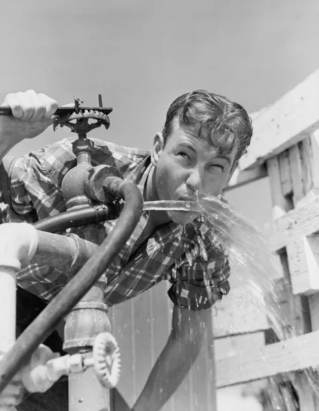 Молодой человек пьет воду из шланга — стоковое фото