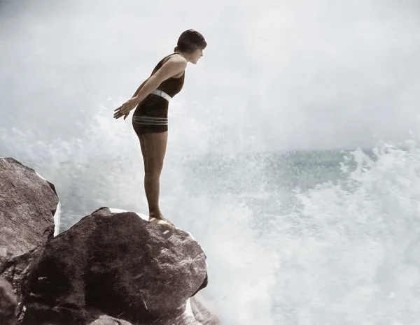 Female swimmer on rock above crashing surf — Stock Photo, Image