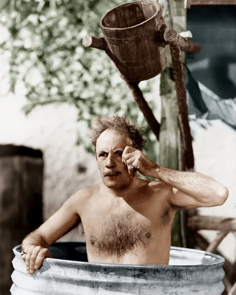Человек, сидящий в бочке, принимающий ванну и смотрящий через свой монокль — стоковое фото