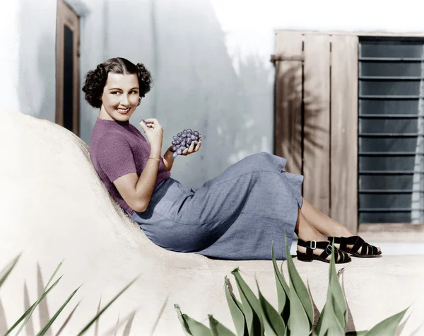 Junge Frau sitzt lächelnd auf einer Terrasse und isst Weintrauben — Stockfoto