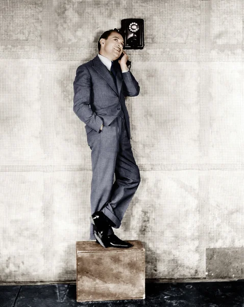 El hombre de pie en una caja para llegar al teléfono — Foto de Stock