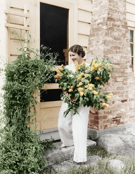 Mujer frente a su casa recogiendo flores en sus brazos — Foto de Stock