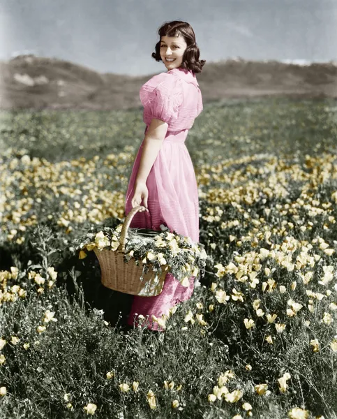 Bir kız ayakta tutan bir çiçek sepeti ve gülümseyen bir çayırda dikiz — Stok fotoğraf