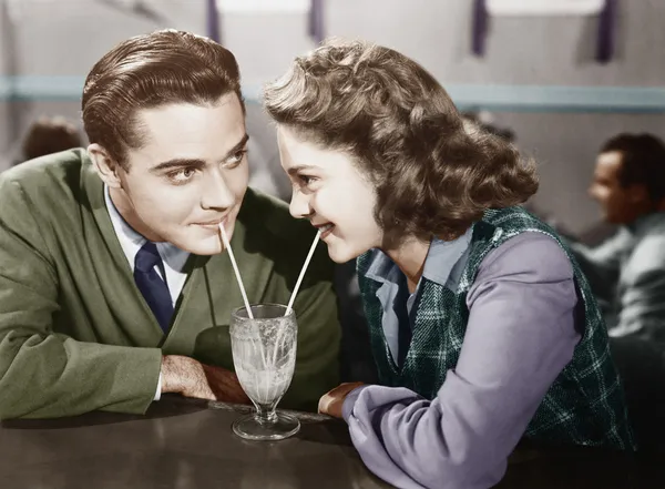 Par i en restaurang tittar på varandra och dela en mjölk shake med två sugrör — Stockfoto
