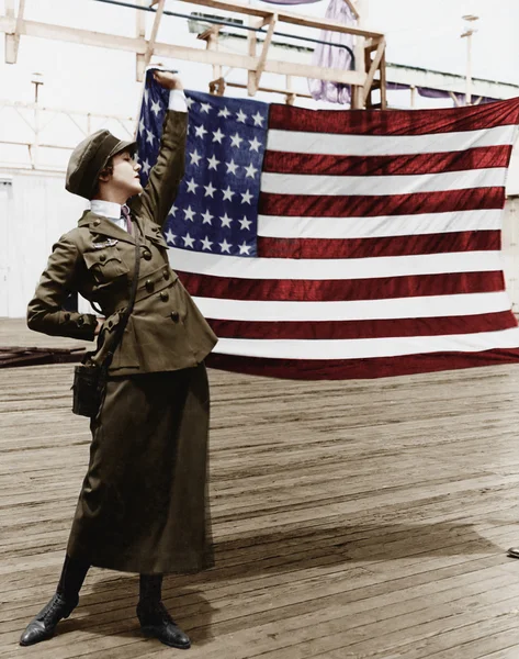 Νεαρή γυναίκα με στρατιωτική στολή που κρατά ψηλά μια αμερικανική σημαία — Φωτογραφία Αρχείου