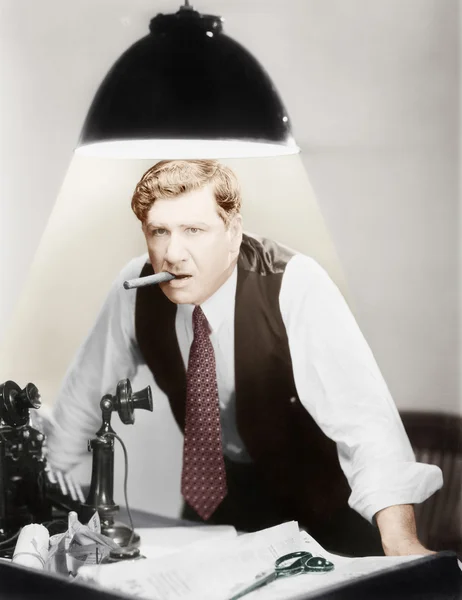 Un uomo appoggiato a una scrivania con una plafoniera che lo illumina — Foto Stock