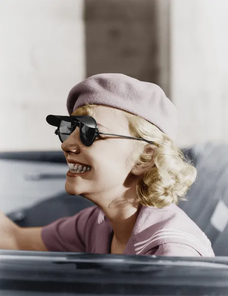 Νεαρή γυναίκα με μπερέ και γυαλιά ηλίου σε ένα αυτοκίνητο, εν κινήσει — Φωτογραφία Αρχείου