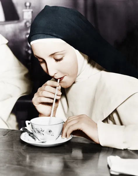 Монахиня потягивает чай из чашки с соломинкой — стоковое фото